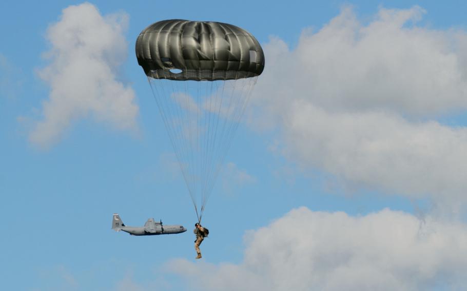A C-130J Super Hercules passes behind a Latvian military member during a combined jump day on June 15, 2015, at Lielvarde Air Base, Latvia. More than 70 U.S. Air Force, U.S. Army and Latvian servicemembers participated in a jump day during exercise Saber Strike 15.