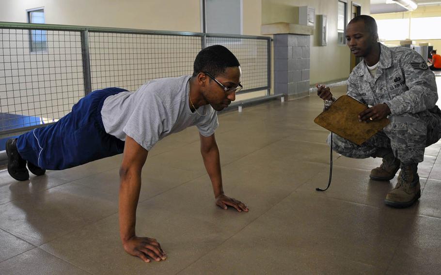 Staff Sgt. Derrick Savoy watches the clock as Airman 1st Class Michael Canady does pushups for one minute on Barksdale Air Force Base, La., Dec. 17, 2013. The Air Force has postponed its fitness requirements until Oct. 1, 2020, due to the coronavirus.