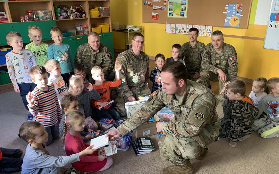 Army Sgt. Timothy Hamlin, front, hands out school supplies to children at the Miejskie Przedszkole school in Elk, Poland, Feb. 5, 2020.