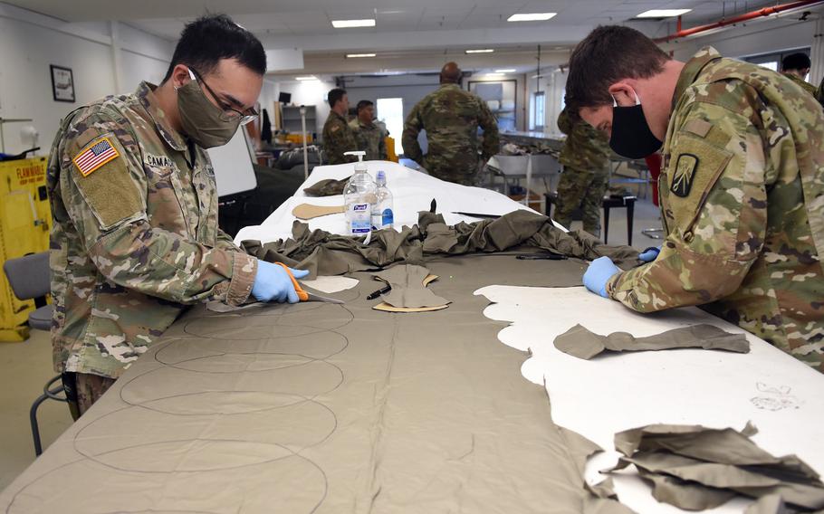 Sgt. Jonathan Camacho, left, and Staff Sgt. Kyle Shields, parachute riggers with the 5th Quartermaster-Theater Aerial Delivery Company at Rhine Ordnance Barracks, Germany, cut out fabric to be sewed into face masks on Wednesday, April 15, 2020. The soldiers are using bedsheets purchased from local base exchanges for materials.