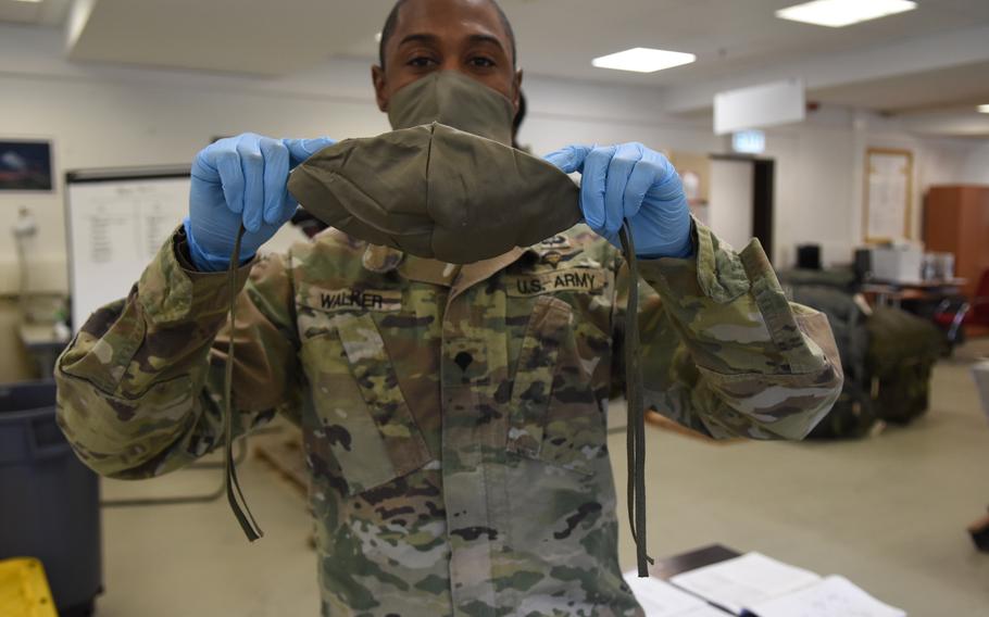 Spc. Robert Walker, a parachute rigger with the 5th Quartermaster-Theater Aerial Delivery Company at Rhine Ordnance Barracks, Germany, holds up one of the masks he and fellow parachute riggers made this week from bed sheets and parachute rigging.