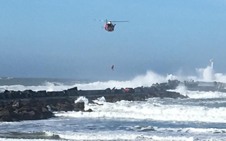 A Coast Guard MH-65 Dolphin helicopter crew from Coast Guard Sector Humboldt Bay hoists a man from Humboldt Bay's north jetty on Jan. 26, 2017, after he became stranded due to a disabled vehicle and hazardous surf conditions.
