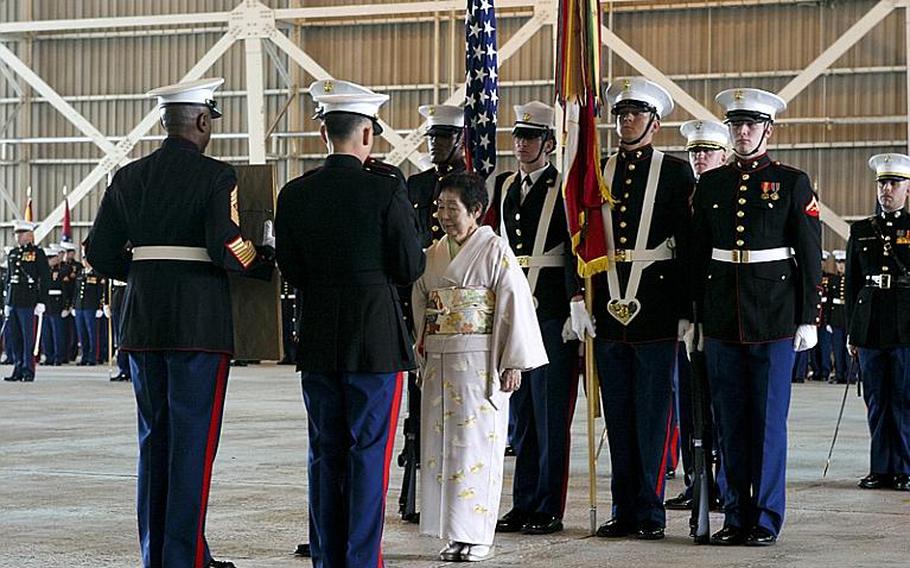 Machiko Hamamoto, Honorary Marine recipient, stands before Sgt. Maj. Gerard Calvin, Marine Aviation Logistics Squadron 12 sergeant major, and Lt. Col. Charles Redden, MALS-12 commanding officer, as they present her a plaque Tuesday recognizing her designation as an Honorary Marine at the Strike Fighter Squadron 94 hangar at Marine Corps Air Station Iwakuni. Hamamoto is a "volunteer-in-readiness," delivering gifts to orphanages and disabled children, organizing relief efforts and local community relation events.