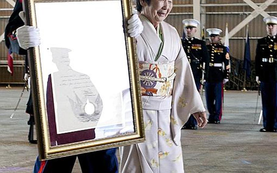 Cpl. Matthew Doyle, Marine Aviation Logistics Sqaudron 12 community relations coordinator, escorts Machiko Hamamoto, Honorary Marine recipient, back to her seat Tuesday, while he carries her Honorary Marine plaque, during a ceremony recognizing her designation as an Honorary Marine at the Strike Fighter Squadron 94 hangar at Marine Corps Air Station Iwakuni. Hamamoto has helped to bolster the relationship between the U.S. military and local Japanese community. Her influence reaches to the U.S. as well. She received an American Red Cross certificate of appreciation for her role in delivering Red Cross services after the 1989 Loma Prieta earthquake near San Francisco.