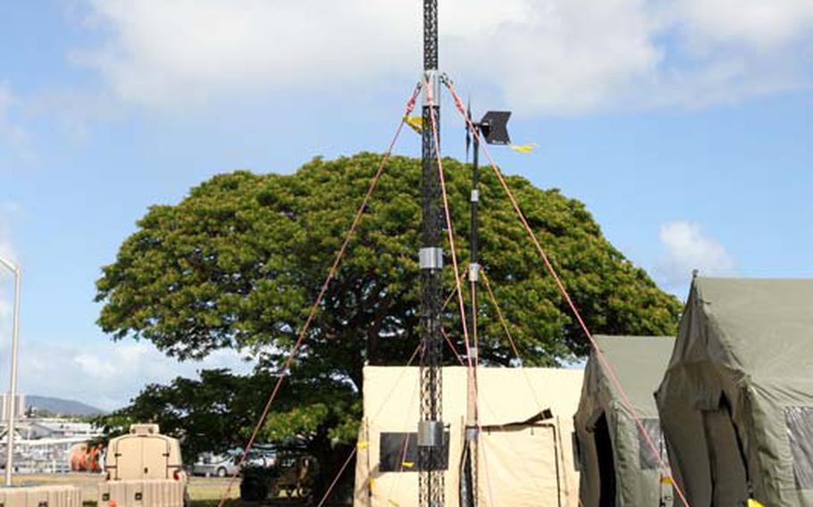 A mobile wind tower used during the Rim of the Pacific exercises Saturday, July 12, 2014, can create enough energy for troops occupying 1 tent. On the ground beside it are foldable solar sheets.