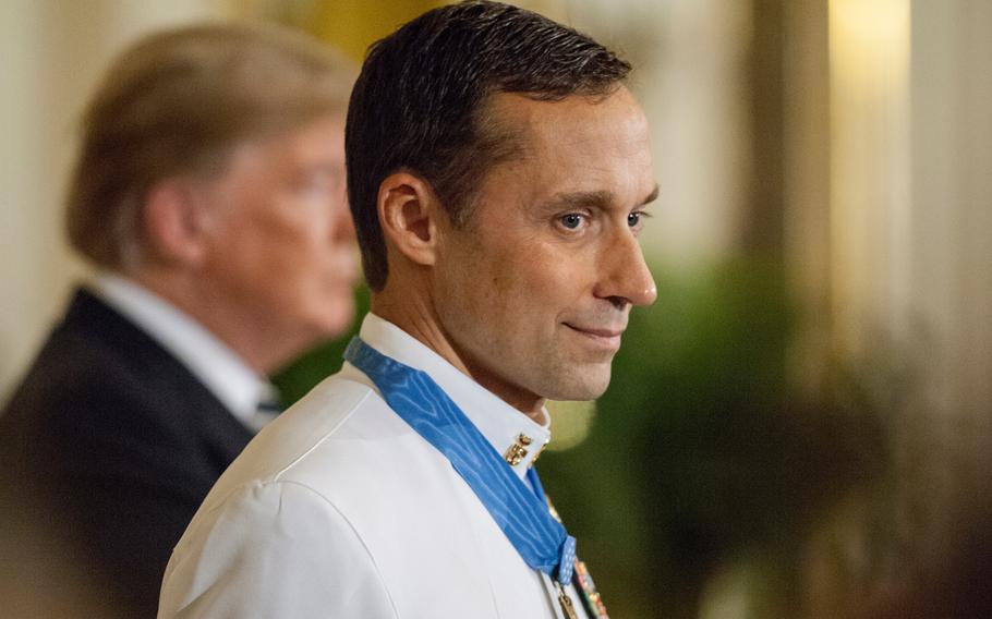 Retired Navy SEAL Master Chief Petty Officer Britt Slabinski grins as he looks towards the crowd after being presented the Medal of Honor at the White House in Washington, D.C., on Thursday, May 24, 2018, during a ceremony in which President Donald Trump, in background, recognized Slabinski for his bravery and heroic actions in what is known as the Battle of Roberts Ridge in Afghanistan in March 2002.