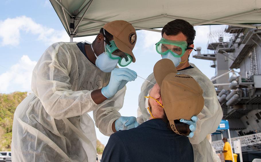 Christian Akins, left, from Atlanta, and Austin Brunt, from Charleston, S.C., assigned to Naval Hospital Guam, take a nasal sample from a U.S. sailor assigned to the aircraft carrier USS Theodore Roosevelt (CVN 71) as part of a public health outbreak investigation on April 23, 2020. 