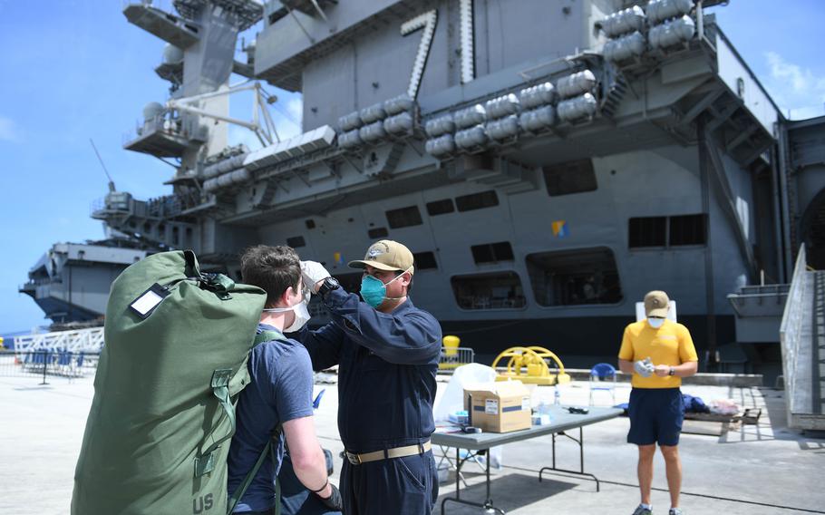 U.S. Navy Senior Chief Hospital Corpsman Elwin Familiar, assigned to the aircraft carrier USS Theodore Roosevelt, checks a sailor;s temperature on the pier at Naval Base Guam on April 30, 2020.