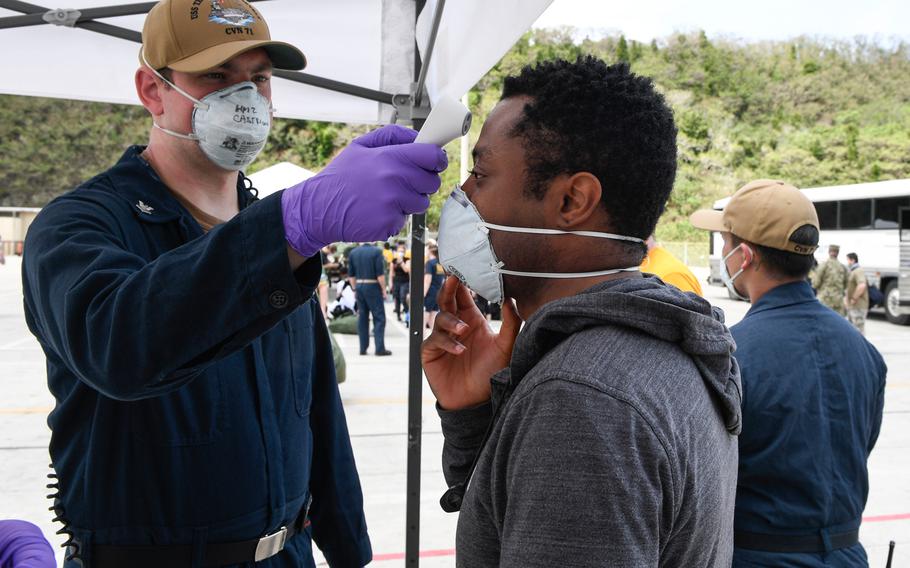 U.S. Navy Hospital Corpsman 2nd Class Jason Castricone, assigned to USS Theodore Roosevelt, checks the temperature of Mass Communication Specialist Seaman Alexander Williams on May 1, 2020. 