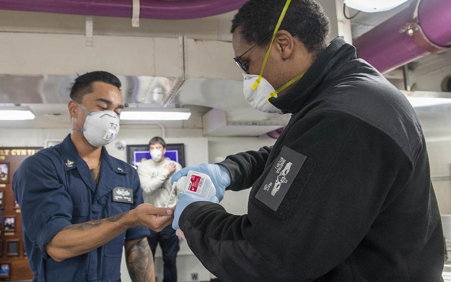 U.S. Navy Electronics Technician 1st Class Demetrius Peavy, right, dispenses hand-sanitizer to U.S. Navy Yeoman 2nd Class Edmond Torrejas aboard the aircraft carrier USS Theodore Roosevelt during an ice cream social on May 23, 2020.