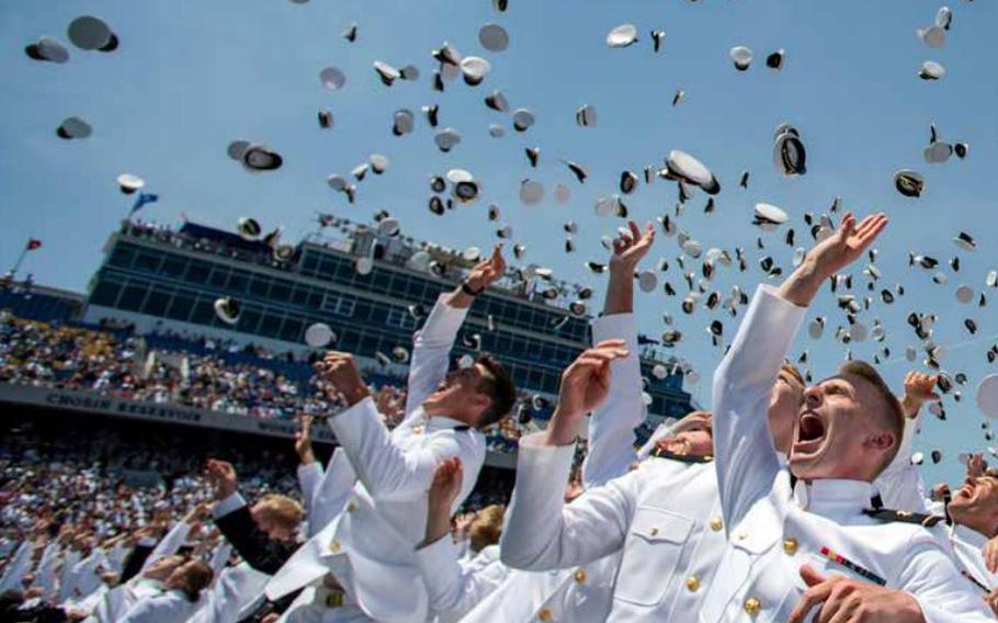 Naval Academy cadets toss their hats in celebration during a graduation ceremony.