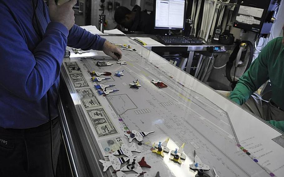 A sailor on board the carrier USS George H.W. Bush moves a jet to match its real-life counterpart on the flight deck using the "Ouija Board," a tapletop model of the ship that has been used to track aircraft movement on carriers since World War II. Small bolts on the model aircraft are stood up or laid on their sides to signify fuel status. The "Ouija Board" is gradually being phased out by the Navy, and all carriers are expected to have an electronic replacement by 2015.
