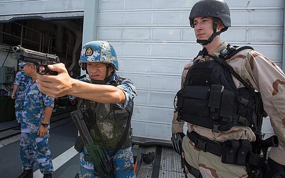 Petty Officer 2nd Class Tristan McAnaney, an electronics technician and member of the onboard search-and-seizure team from the guided-missile destroyer USS Mason, watches as a Chinese sailor gets a feel for the Beretta M9 pistol during a combined small-arms exercise aboard the Chinese destroyer Harbin in the Gulf of Aden on Aug. 24, 2013.

