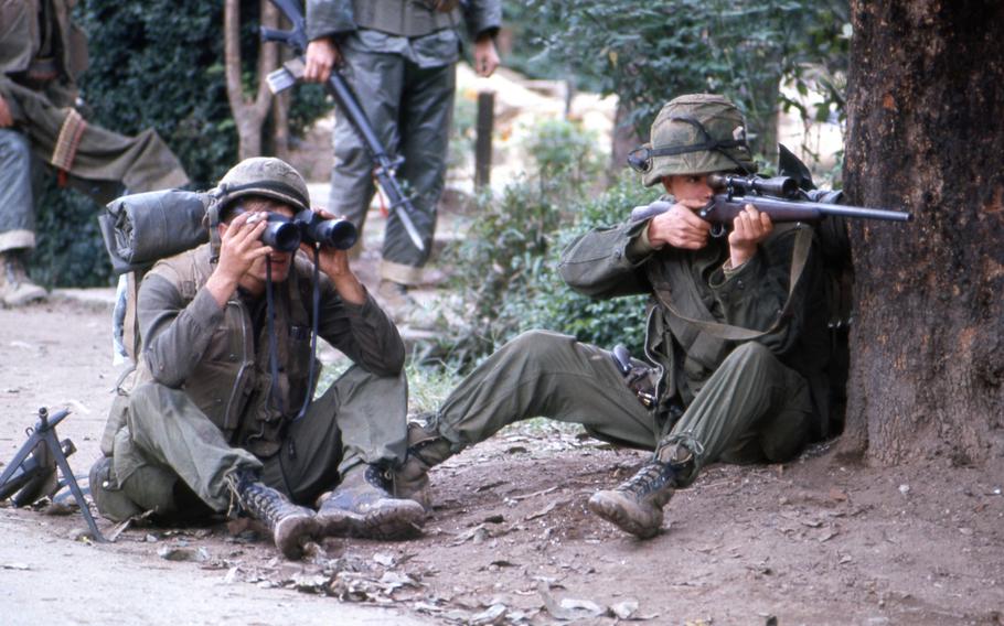 A Marine sniper takes aim from behind a tree as his comrade looks through a pair of binoculars to establish the enemy position in Hue during the battle for the city in 1968.