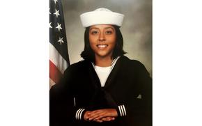 Angelina Resendiz poses in her Navy uniform with an American flag behind her right shoulder.