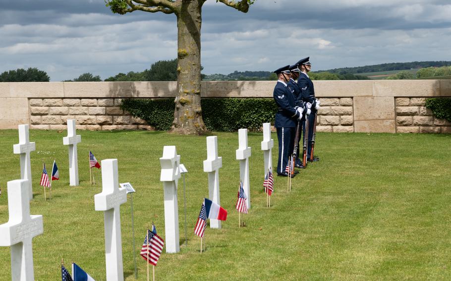 Troops stand at attention, guns in front, among the grave markers.