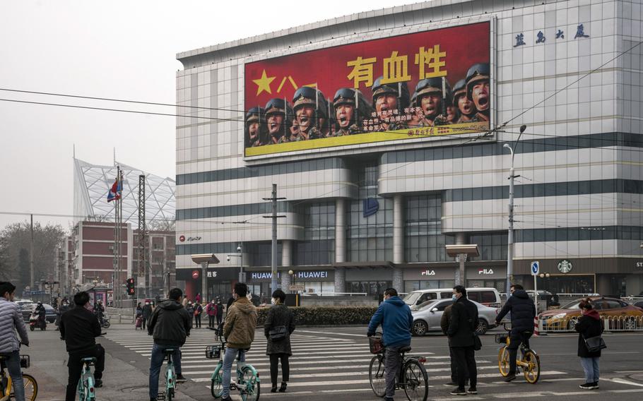 Pedestrians and cyclists stand in front of a screen showing an advertisement for the People's Liberation Army in Beijing on March 5, 2021. 