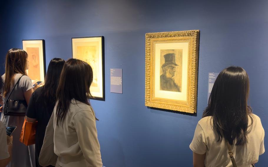People examine art portraits hanging on a museum wall.