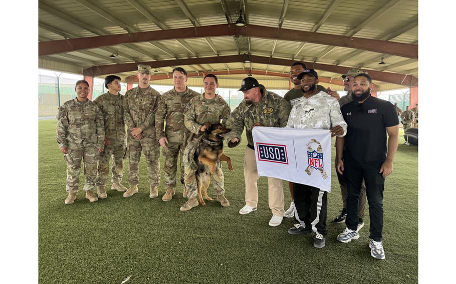 A group of service members and two NFL players hold a USO banner and pose for a photo