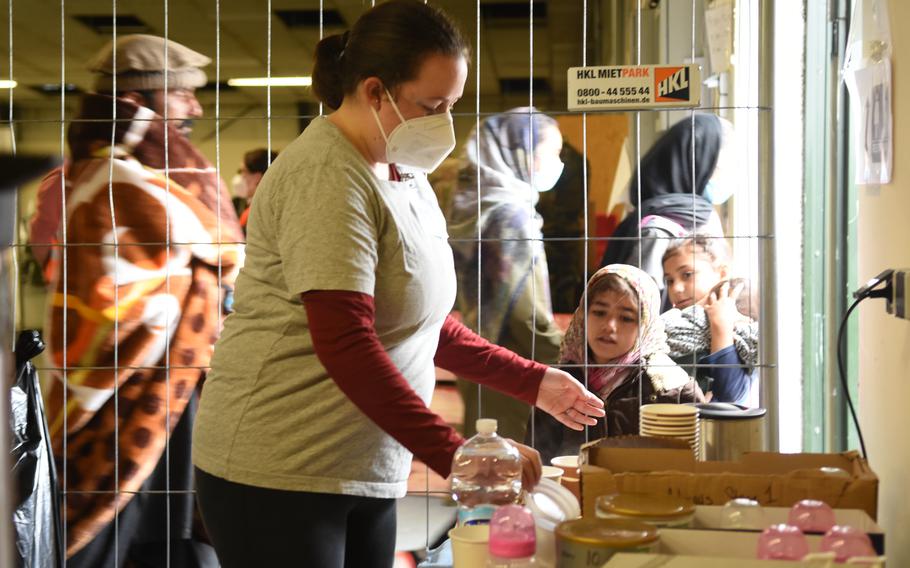 Volunteer Erin Shah grabs a lid at the formula and tea station at Rhine Ordnance Barracks, Germany, on Sept. 20, 2021. Afghan children watch intently while she works.