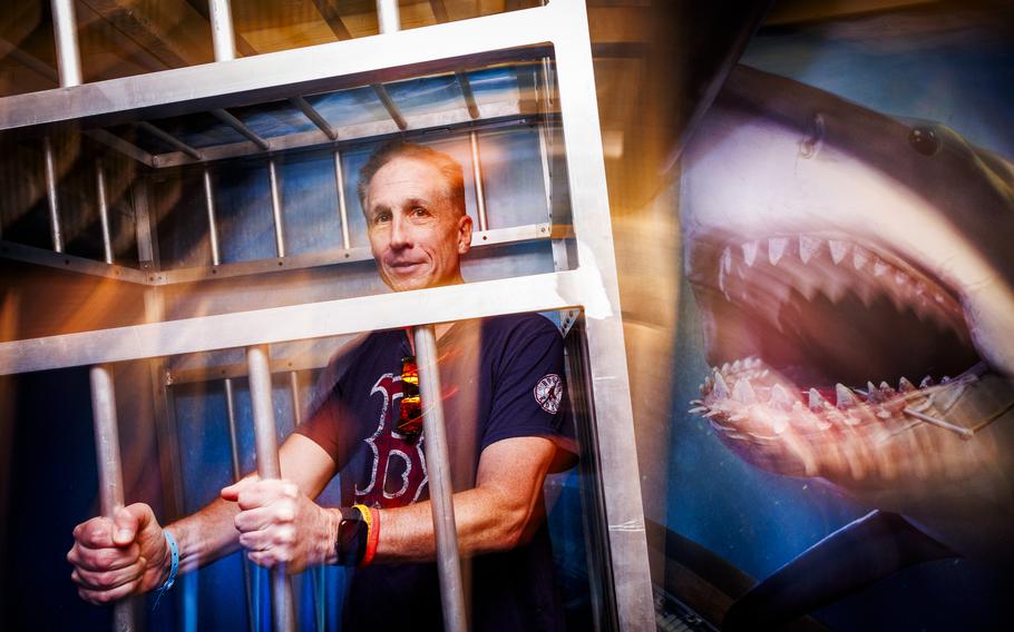 A man poses for a photo in a faux shark cage.