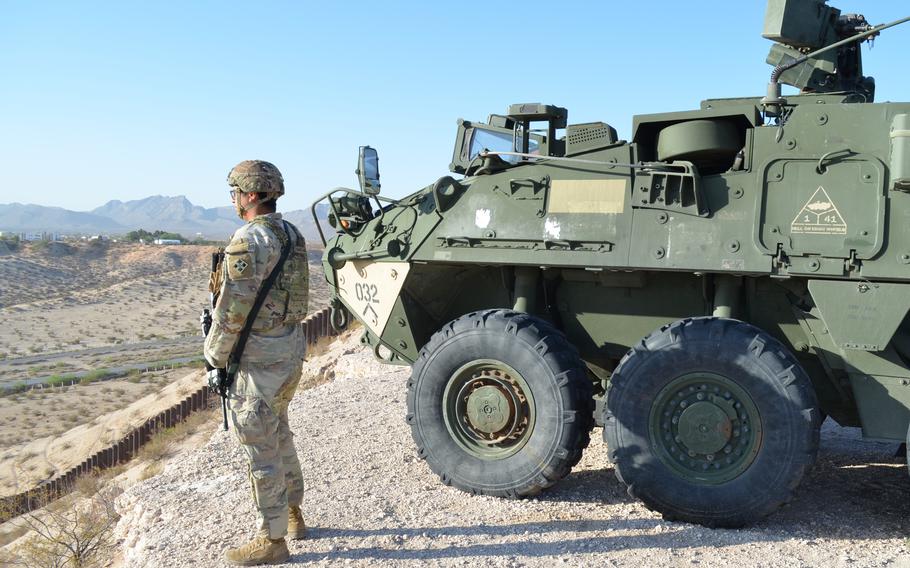 A soldier standing next to a military vehicle watches over a desolate valley.