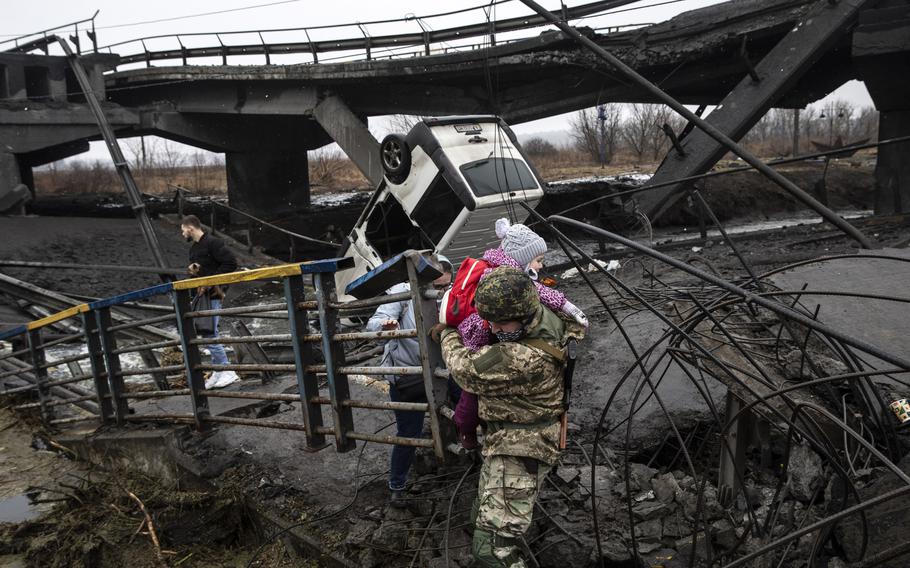 A Ukrainian commander carries a young girl as he helps people flee across a destroyed bridge on the outskirts of Kyiv, Ukraine, on Thursday. Ukrainian forces say Russian fighters destroyed the bridge. 