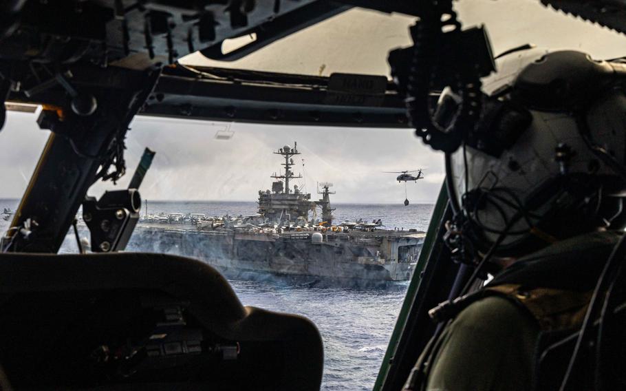 Looking out the window of a military helicopter at an aircraft carrier cruising at sea.