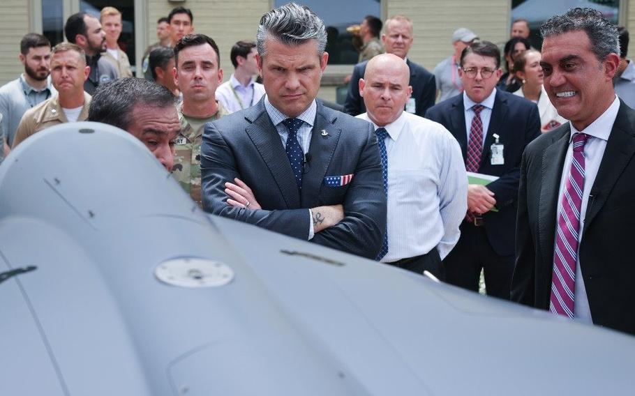 Pete Hegseth makes a face as he looks at a gray drone.