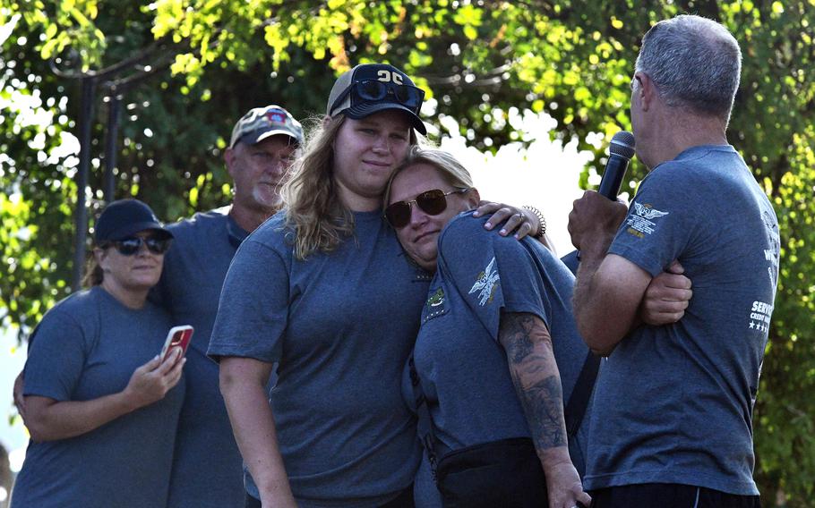 A group of people in matching T-shirts stand close together, some embracing.