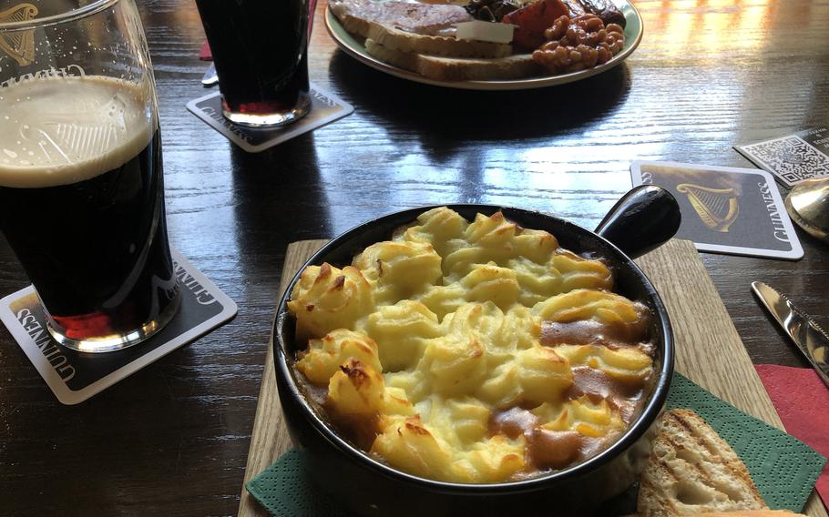 The traditional homemade cottage pie with ground Irish beef, onions, celery and carrots, in a gravy and red wine sauce, topped with mashed potatoes, served with toasted bread and butter and a traditional Irish breakfast in the background. Served at Waxy’s Irish Pub in Frankfurt, Germany.