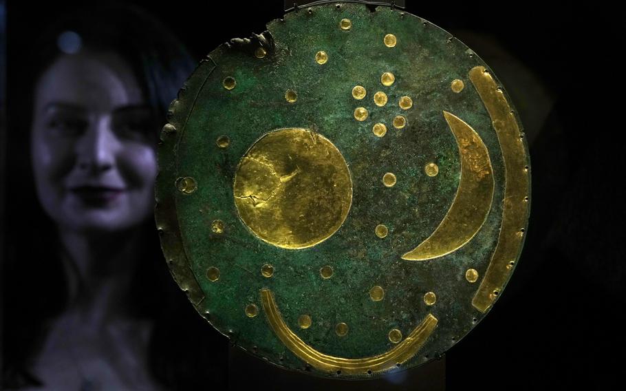 A member of staff poses next to the ‘Nebra Sky Disc’ which dates from around 1600 BCE, and is the oldest surviving representation of the cosmos, on display at the The World of Stonehenge’ exhibition at the British Museum in London, Monday, Feb. 14, 2022. The exhibition which displays objects and artifacts from the era of Stonehenge opens on Feb. 17 and runs until  July 17, 2022. The Nebra Disc was found in Nebra in Saxony-Anhalt in east Germany, in 1999. 