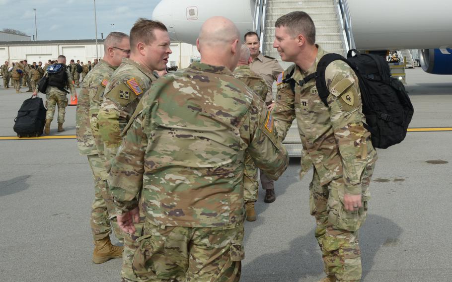 A soldier inclines his body forward slightly to shake hands with his leaders on the tarmac by a plane.