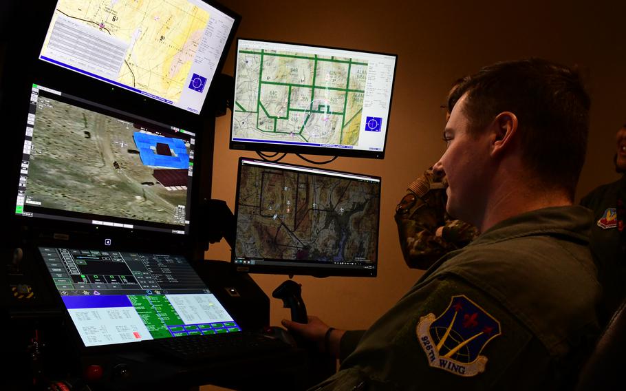 A service member sits and looks at multiple computer screens.