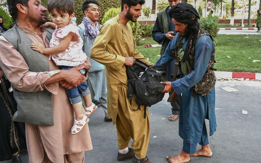 A Taliban fighter, right, searches the bags of people coming out of the Kabul airport in Kabul on Aug. 16, 2021. 