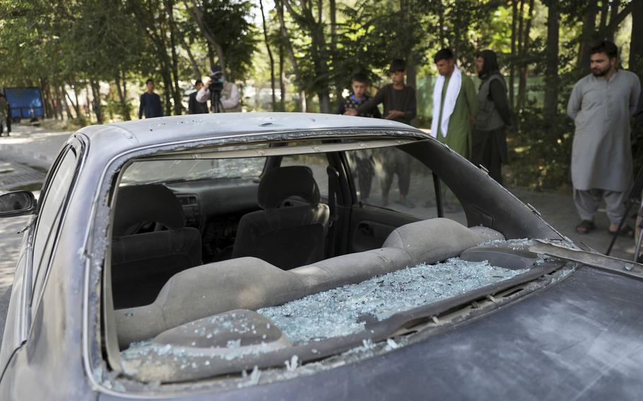 Afghan men look at a damage car after a roadside bomb explosion in Kabul, Afghanistan, Sunday, June 6, 2021.