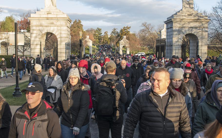 Volunteers pour through the entrance gate at Arlington National Cemetery to help place more than a quarter-million wreaths on veteran tombstones on Saturday, Dec. 17, 2022.