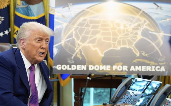Donald Trump sits at a desk next to a poster on an easel reading “Golden Dome for America” with an artist’s rendering of a gold-colored defense dome over a map of the United States.