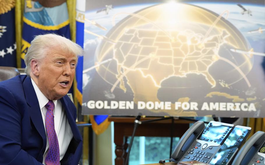 Donald Trump sits at a desk next to a poster on an easel reading “Golden Dome for America” with an artist’s rendering of a gold-colored defense dome over a map of the United States.