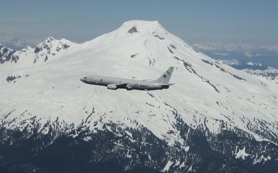 A plane with the U.S. Navy logo flies in front of a snowcapped mountain.