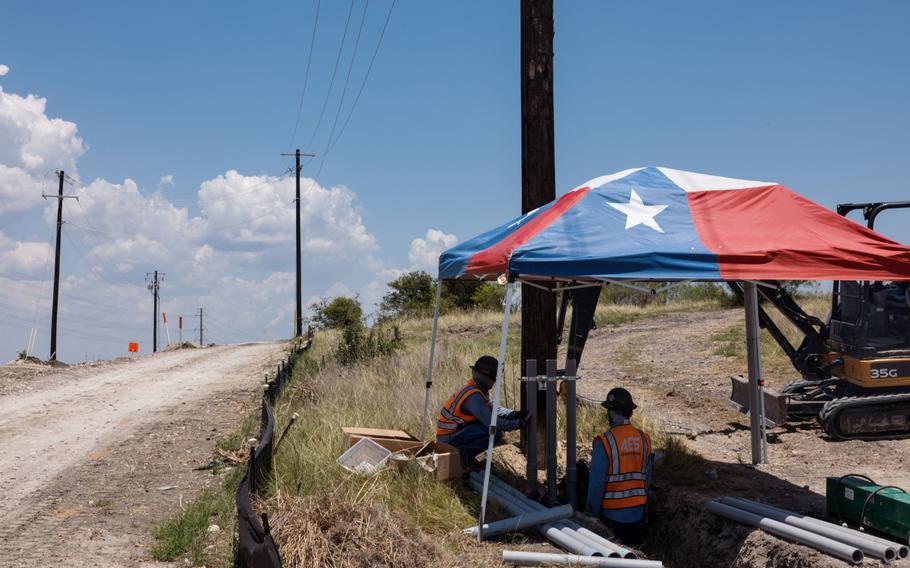 Workers install infrastructure under a Texas flag tent during a heat wave in Austin on July 11, 2022. 