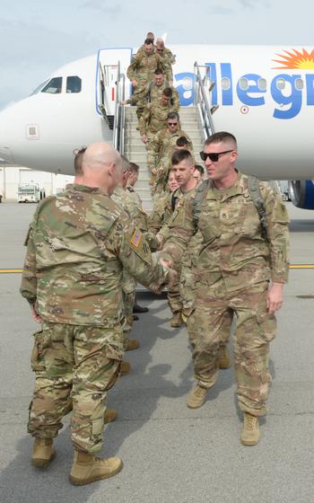 A vertical photo of soldiers shaking hands with their leaders on the tarmac in front of a plane.