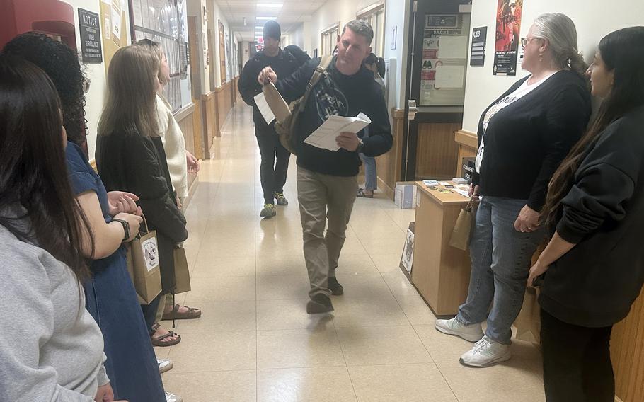 A man wearing khaki pants, a black hooded sweatshirt and a backpack walks down a hallway lined with volunteers.