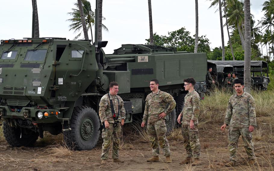 U.S. soldiers wearing uniforms gather in front of military vehicles.