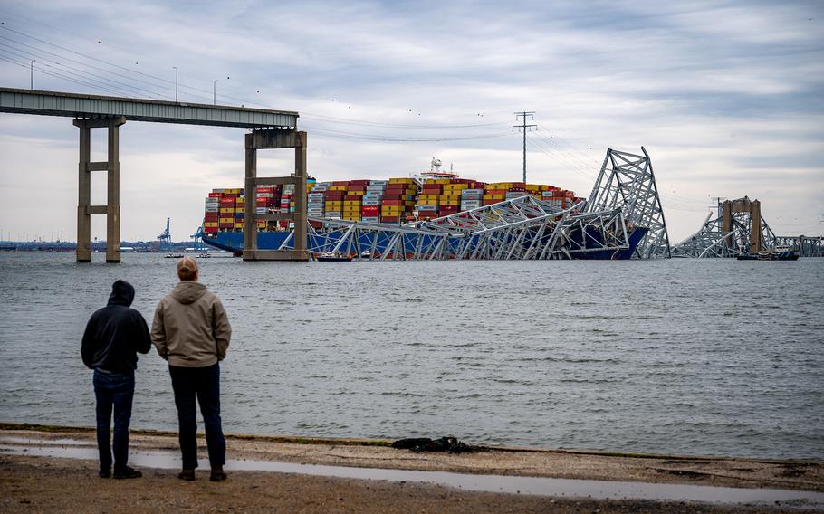 Two men at Fort Armistead Park look at the twisted structure and road decking from the Francis Scott Key Bridge that are draped across the bow of the container ship Dali on March 28, 2024. 