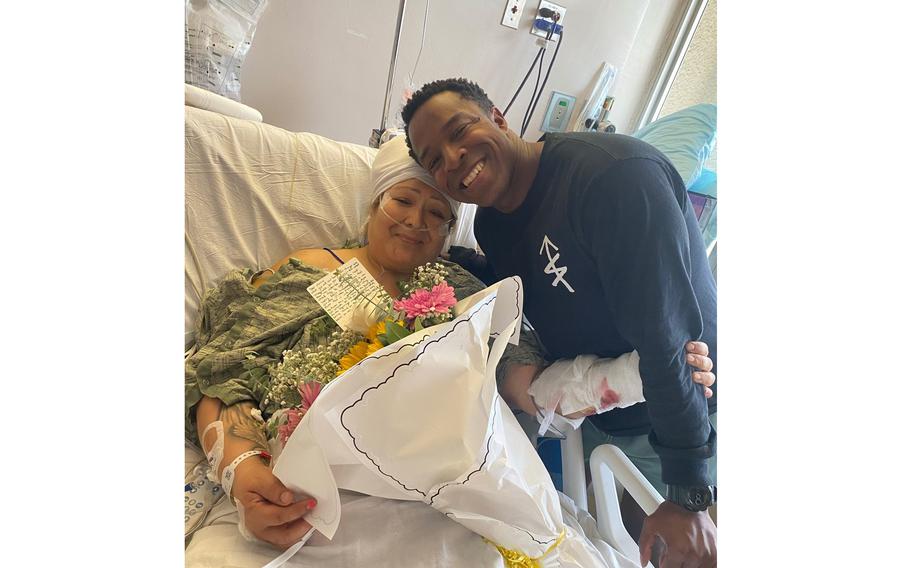 A man poses with a woman in a hospital bed.