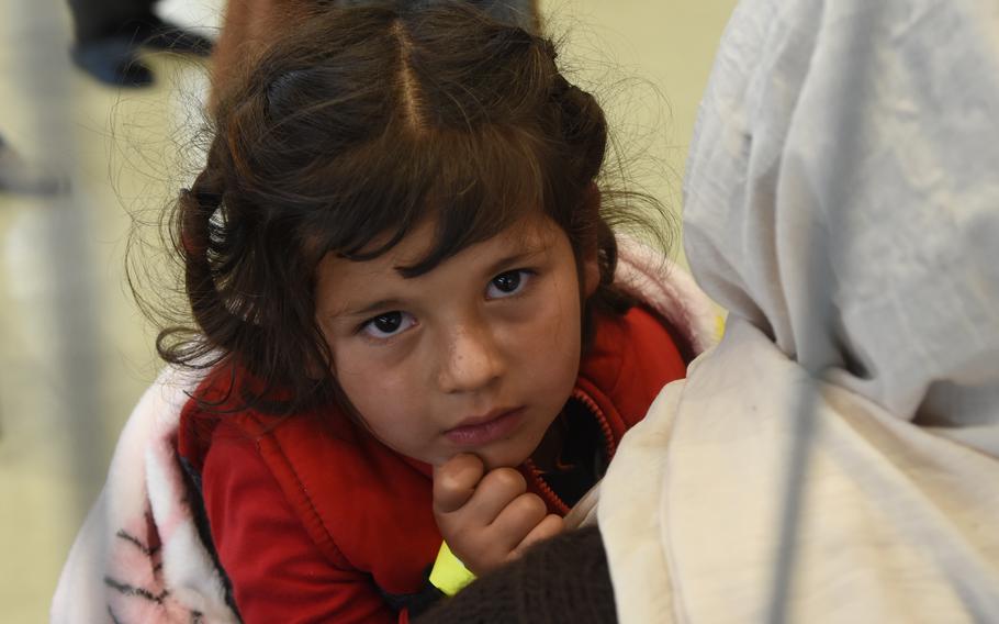 A little girl is held while sitting inside a makeshift passenger terminal for evacuees from Afghanistan who are waiting for a flight to the United States from Ramstein Air Base, Germany, Aug. 26, 2021. The number of inbound evacuees is far exceeding the number of outbound passengers.