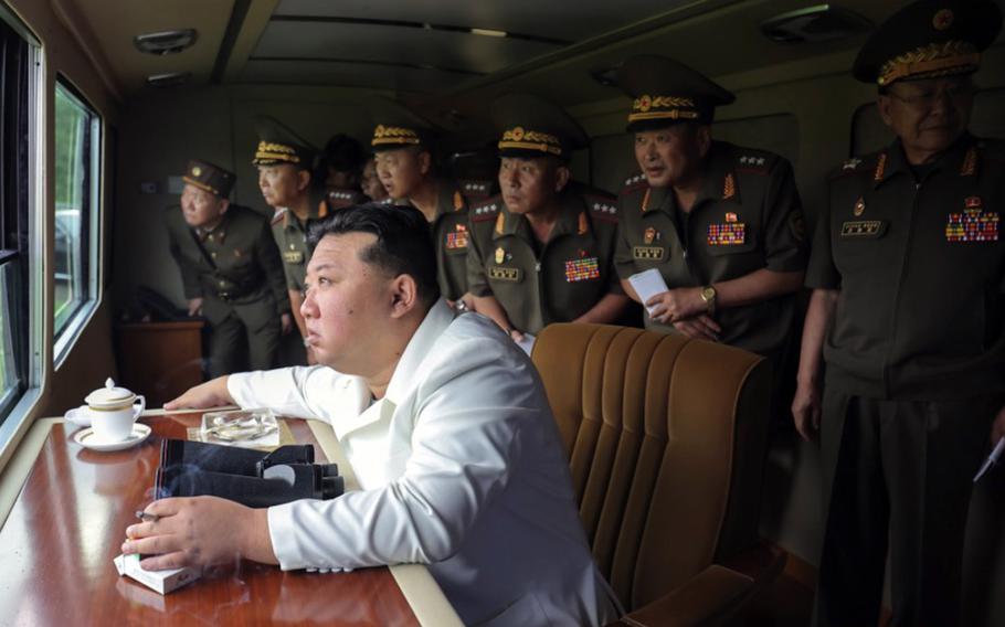 Kim Jong Un, surrounded by North Korea soldiers, looks out a window to observe weapons testing.