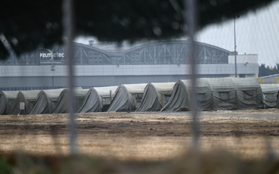 A tarp lining the fence is blown by the wind, revealing a long row of military tents that are set up at an airfield on the outskirts of Mielec, Poland, Feb. 26, 2022. 