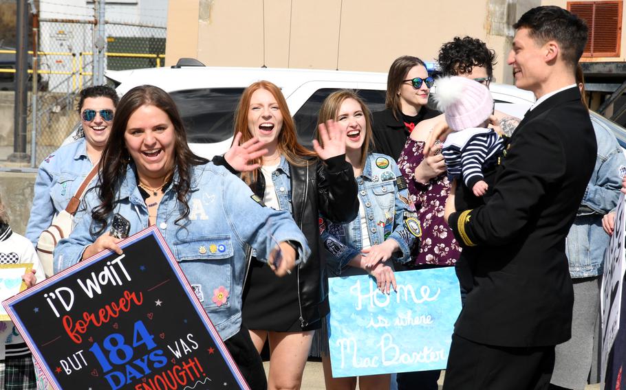 Families and friends, some holding signs, gather on the pier.